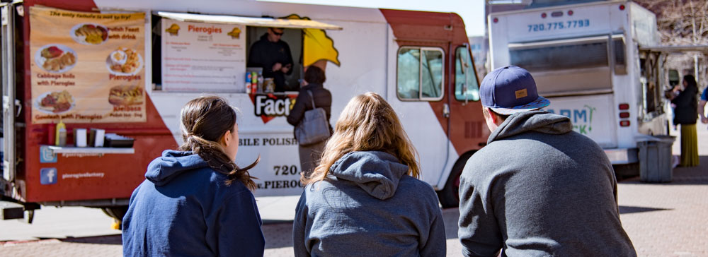 Students sitting on a bench eating near the food trucks