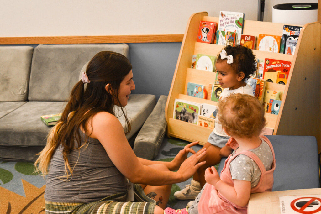 Early Learning Center - Teacher with with two children in front of a bookshelf