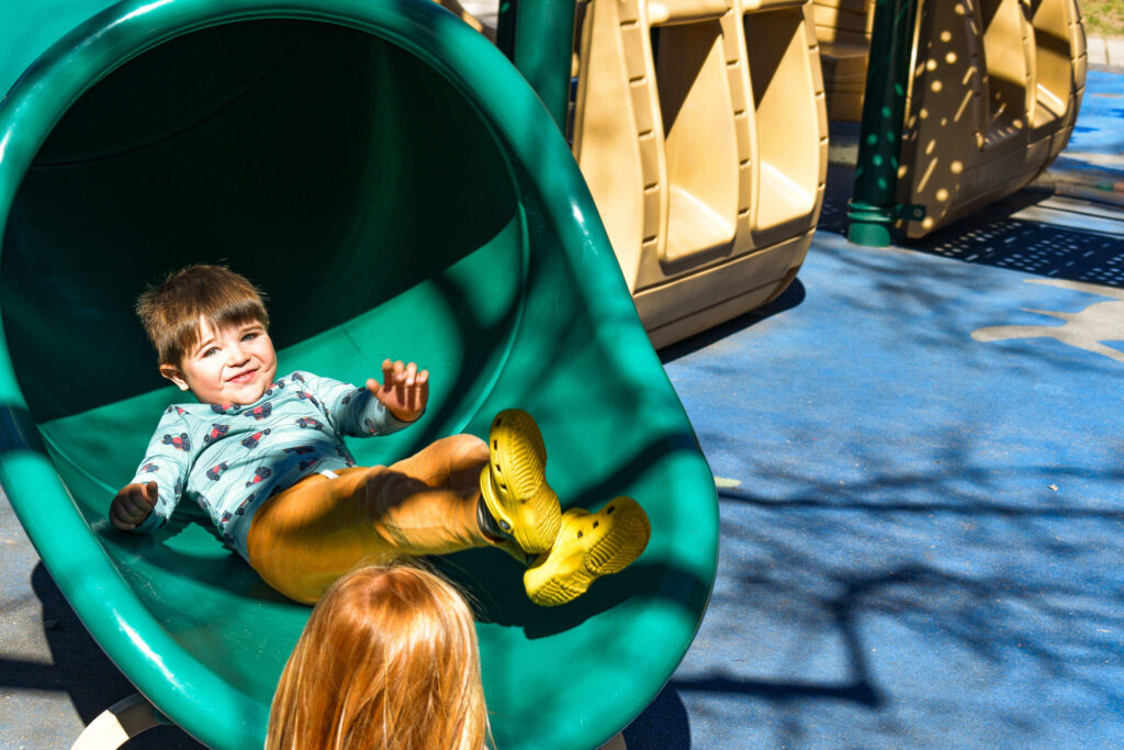 Early Learning Center - Child sliding down a green slide on a playground